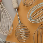 Whisks collection featuring various types and colors on a beige and orange background.