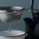 Tea infuser held above a cup with green tea dripping through it.