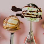 Ice cream scoop holding colorful, decorated ice cream scoops with toppings on a pink background.