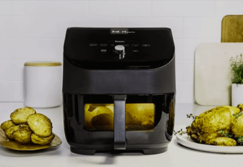 Air Fryers with a viewing window cooking food inside, surrounded by crispy potato slices and a roasted chicken on a kitchen counter.