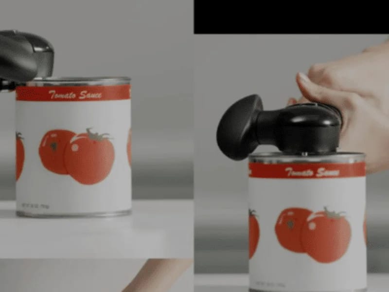 Can Opener in action being used to open a can of tomato sauce with a black ergonomic handle.