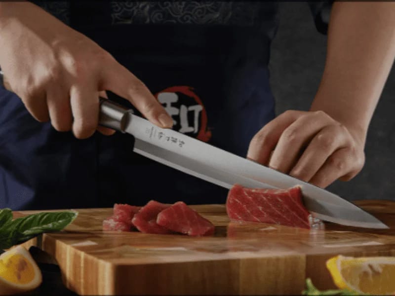 Chef slicing raw tuna with a sharp Japanese-style kitchen knife on a wooden cutting board.