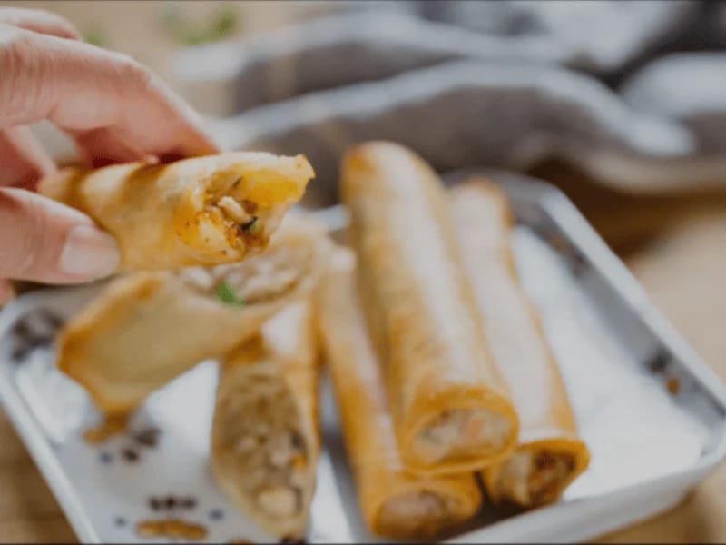 Hamuraki Spring Rolls served on a white plate with a sweet chili dipping sauce, filled with shredded vegetables and golden crispy wrappers.