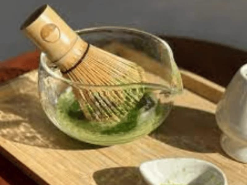 Whisks blending matcha tea in a glass bowl using a traditional bamboo matcha whisk.