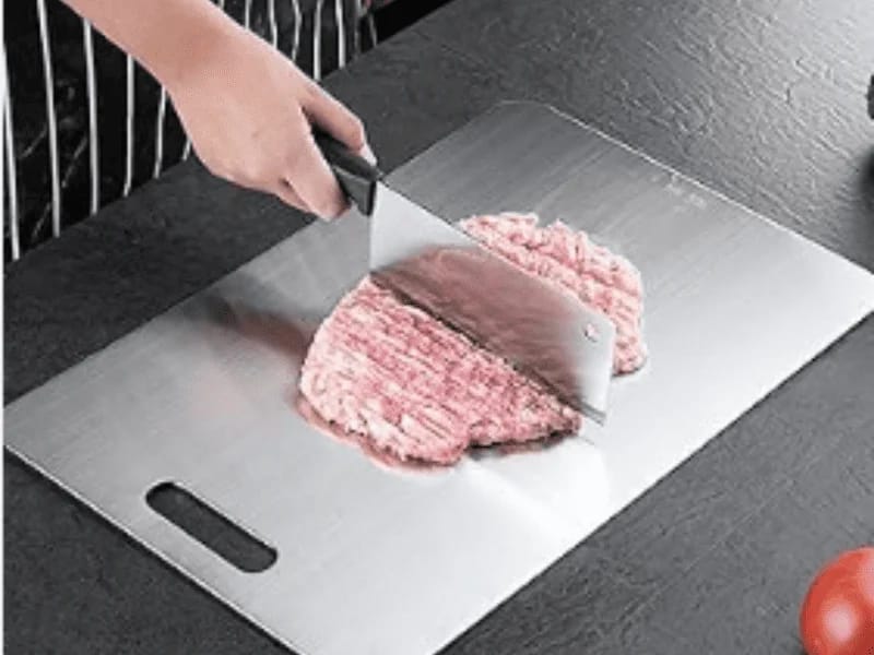 A person chopping minced meat on a stainless steel cutting board with a large cleaver knife