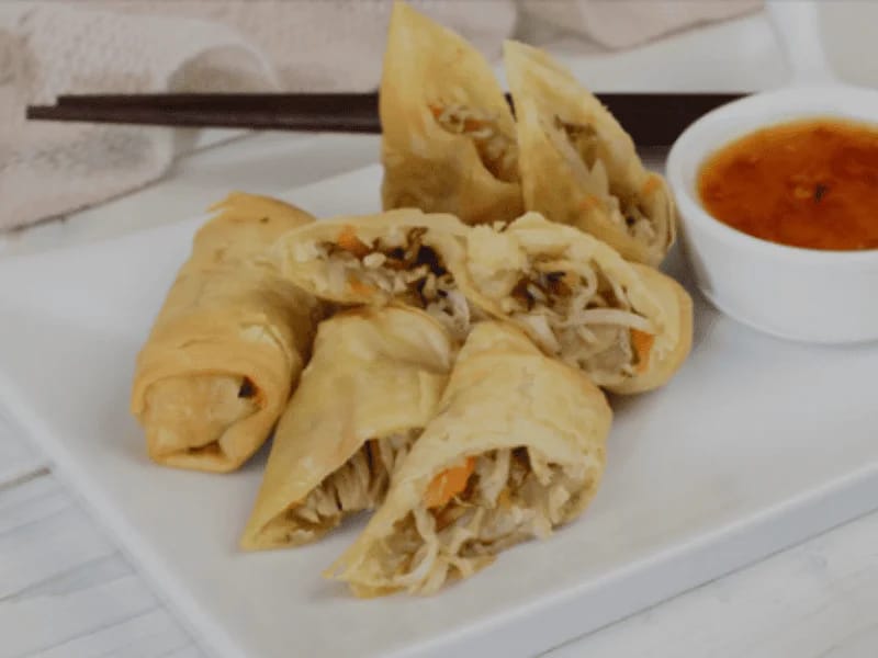 Hamuraki Spring Rolls served on a white plate with a sweet chili dipping sauce, filled with shredded vegetables and golden crispy wrappers.