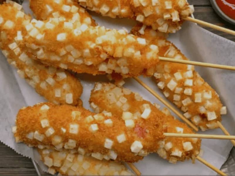 Korean Corn Dog coated in diced potatoes and deep-fried to golden perfection, served on wooden sticks.