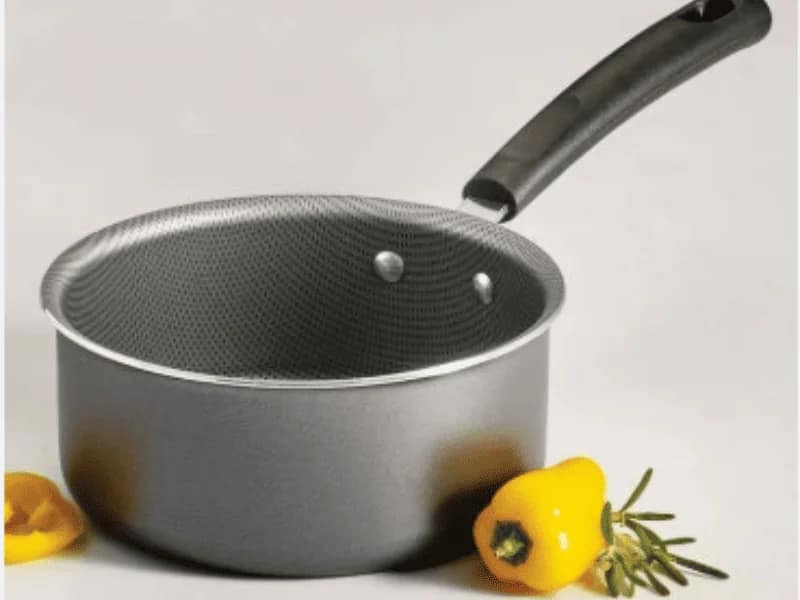 A Sauce Pan with Grey and black handle, placed beside yellow bell pepper and rosemary.