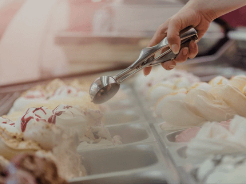 Ice cream scoop being used by hand to serve gelato from a display case in a dessert shop