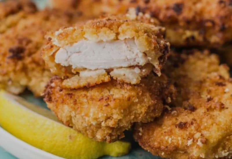 Fried Chicken nugget broken open to reveal juicy white meat inside, served with lemon slices.