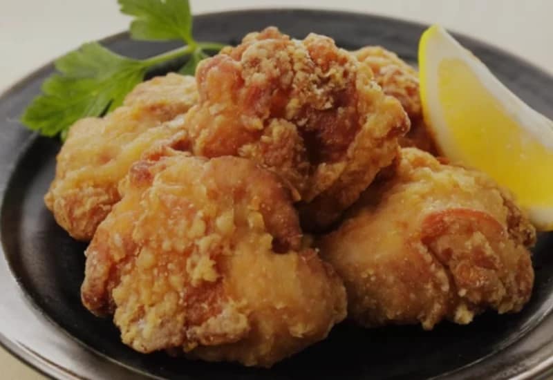 Fried Chicken served on a black plate with a lemon wedge and fresh parsley.