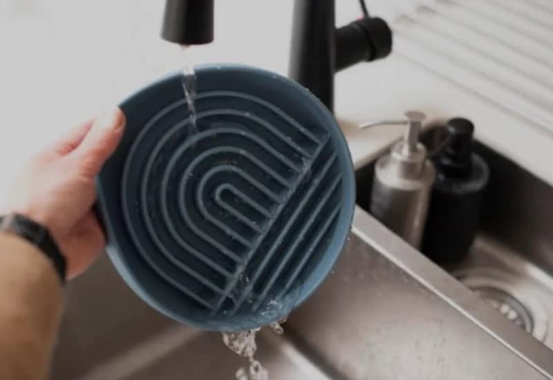 Dog Feed Bowl being rinsed under running water in a kitchen sink.